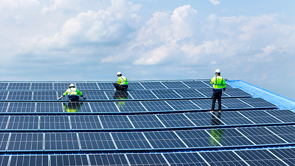 Workers installing or inspecting solar panels on a large rooftop array.