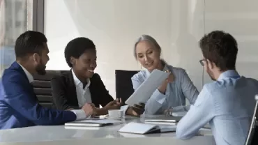 four people sitting in an office and reading a report