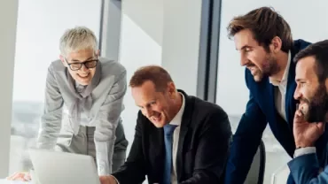 a group of people smiling looking to a computer in an office