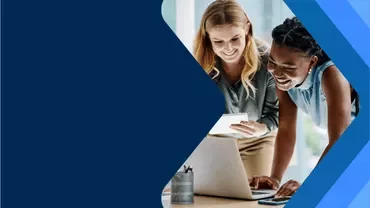 Two people working together at a desk with a laptop, framed by a blue geometric graphic.
