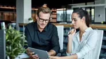 Professionals reviewing information together on a tablet in a workplace setting.
