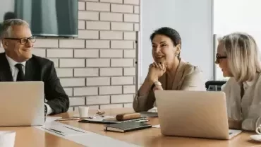 Three colleagues having a meeting at a table with laptops.