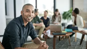 Professional seated in the foreground with colleagues collaborating in the background during a meeting.