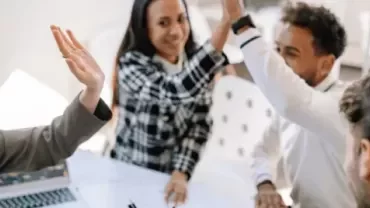 Professionals collaborating during a meeting and celebrating success with a high-five.