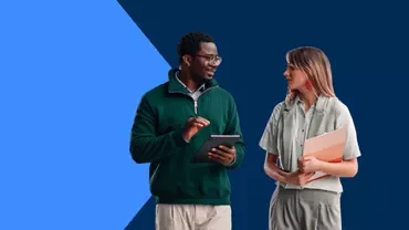 Two professionals standing and discussing while holding a tablet and folder against a blue background