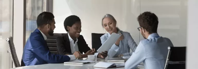 four people sitting in an office and reading a report