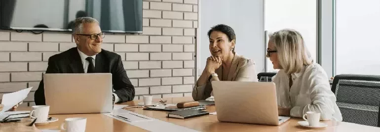 Three colleagues having a meeting at a table with laptops.