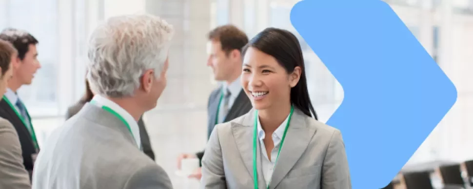 a woman smiling talking with a man with a group of coworkers in the backgorund